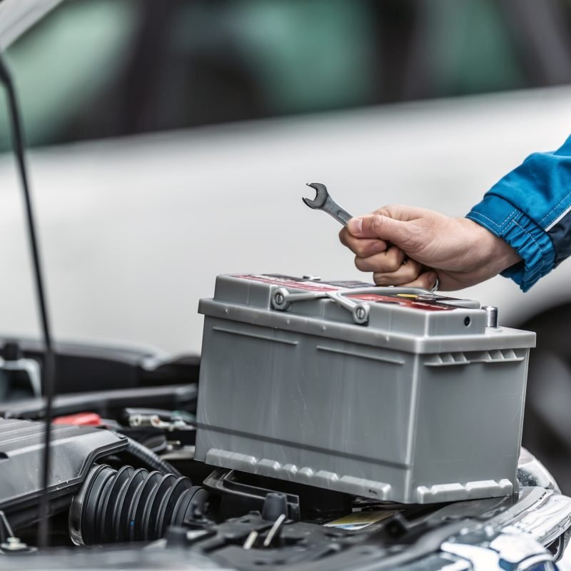 Mechanic holds key over car battery with engine trunk of the car open.